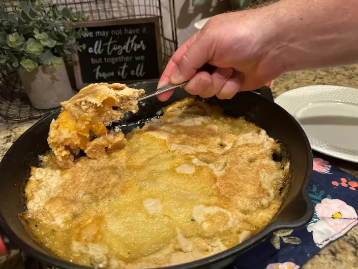 scooping peach cobbler out of cast iron skillet