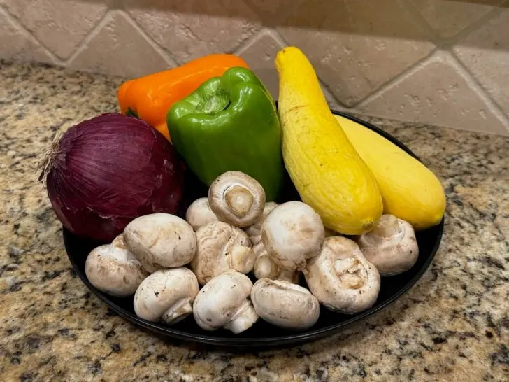 Raw veggies on plate (mushrooms, red onion, squash, peppers)