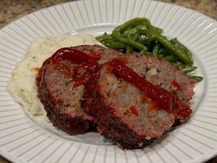 sliced meatloaf on plate with mashed potatoes and green beans