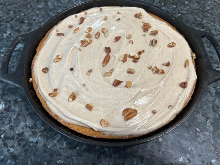pumpkin spice cake, frosted, in cast iron skillet with chopped pecans on top