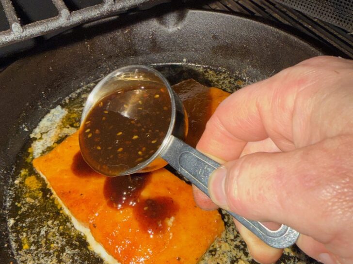 adding seasoning to salmon in skillet