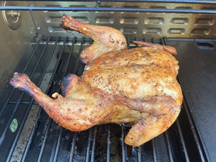 partially cooked spatchcocked chicken on a gas grill