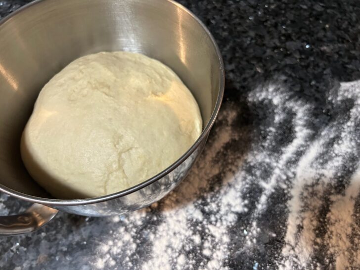 risen bread dough in bowl next to floured surface