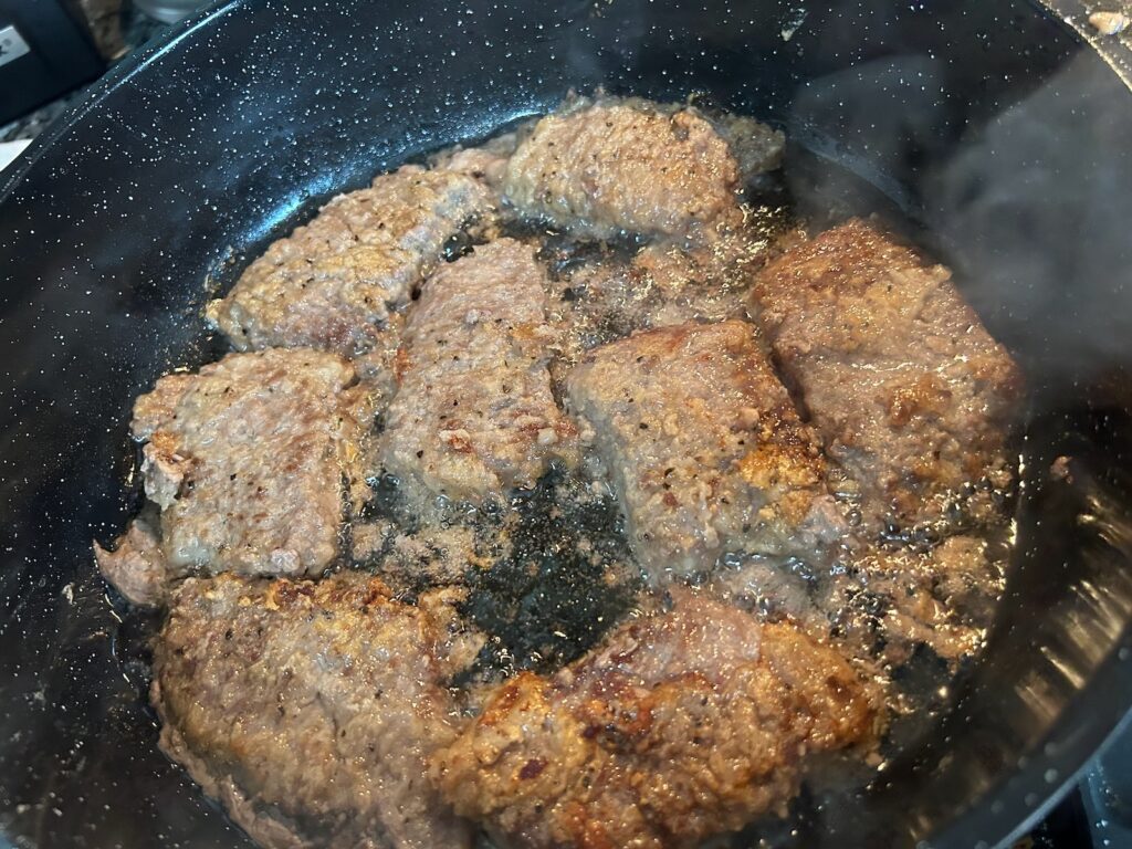 beef pieces frying in skillet