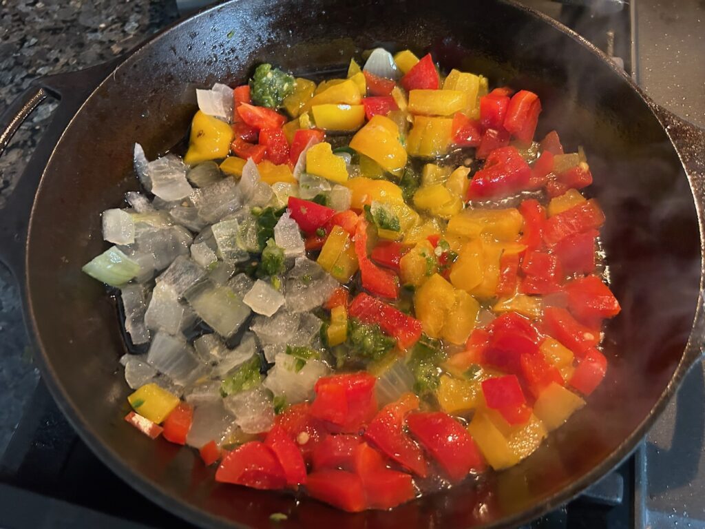 red and yellow peppers simmering in cast iron skillet with onions and jalapenos
