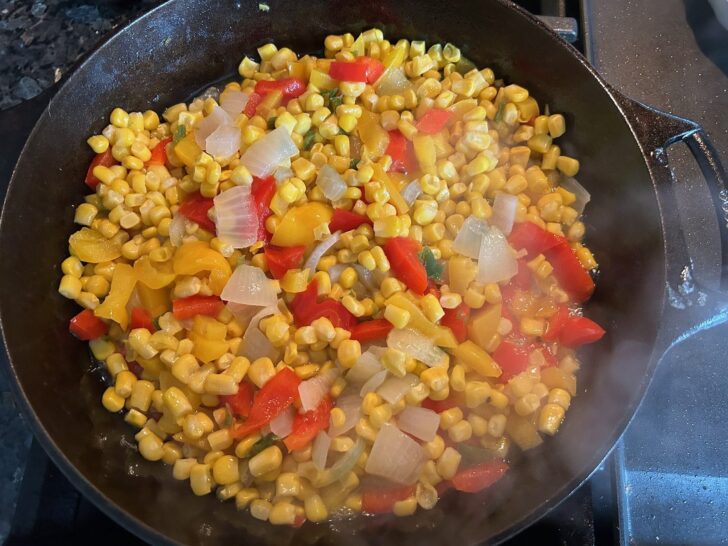 red and yellow peppers simmering in cast iron skillet with onions and jalapenos. Corn added.