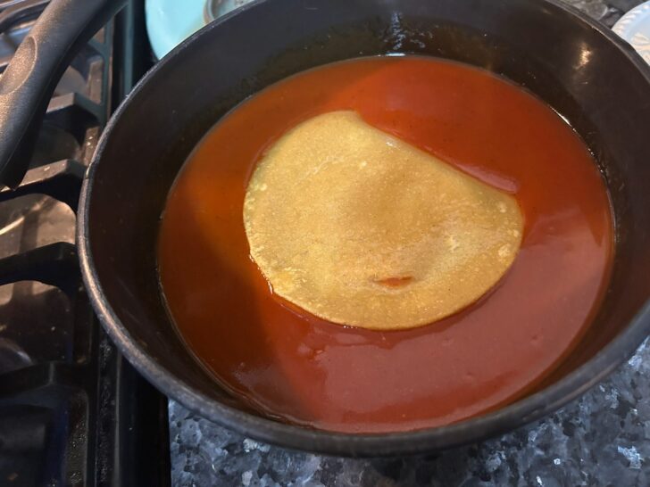 tortilla in bowl of enchilada sauce