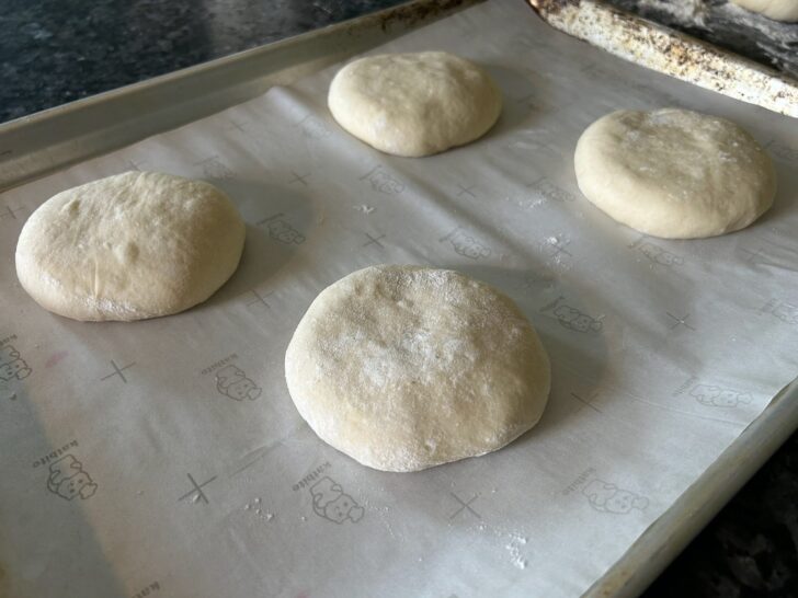buns rising on baking sheet with parchment paper