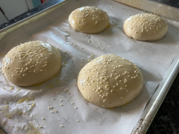 unbaked buns with sesame seeds on tray with parchment paper