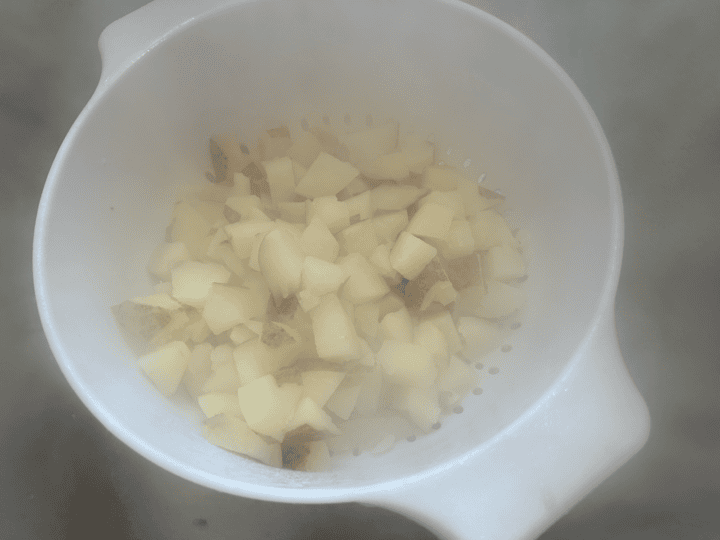 cooked cubed potatoes cooling in strainer